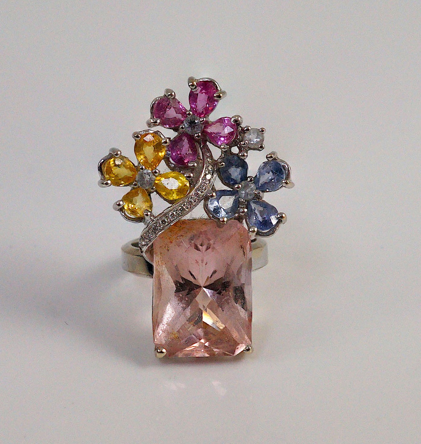 A large modern 14k white gold, morganite, four colour sapphire (including colourless) and diamond chip set triple flower head dress ring, in a raised setting